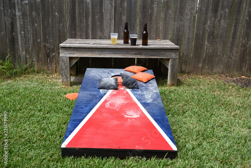 Red, white and blue corn hole game in back yard with dusty bags landing on board