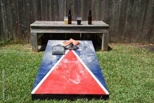 Red, white and blue corn hole game in back yard with dusty bags landing on board