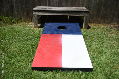 Red, white and blue corn hole game in back yard with dusty bags landing on board
