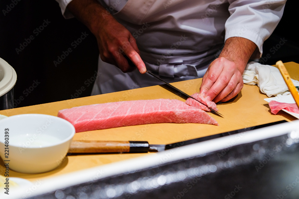 A chef skillfully prepares fresh raw fatty tuna for his customers. A chef skillfully prepares fresh raw fatty tuna for his customers.