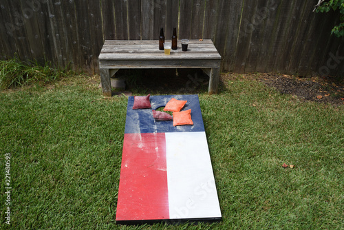 Red, white and blue corn hole game in back yard with dusty bags landing on board