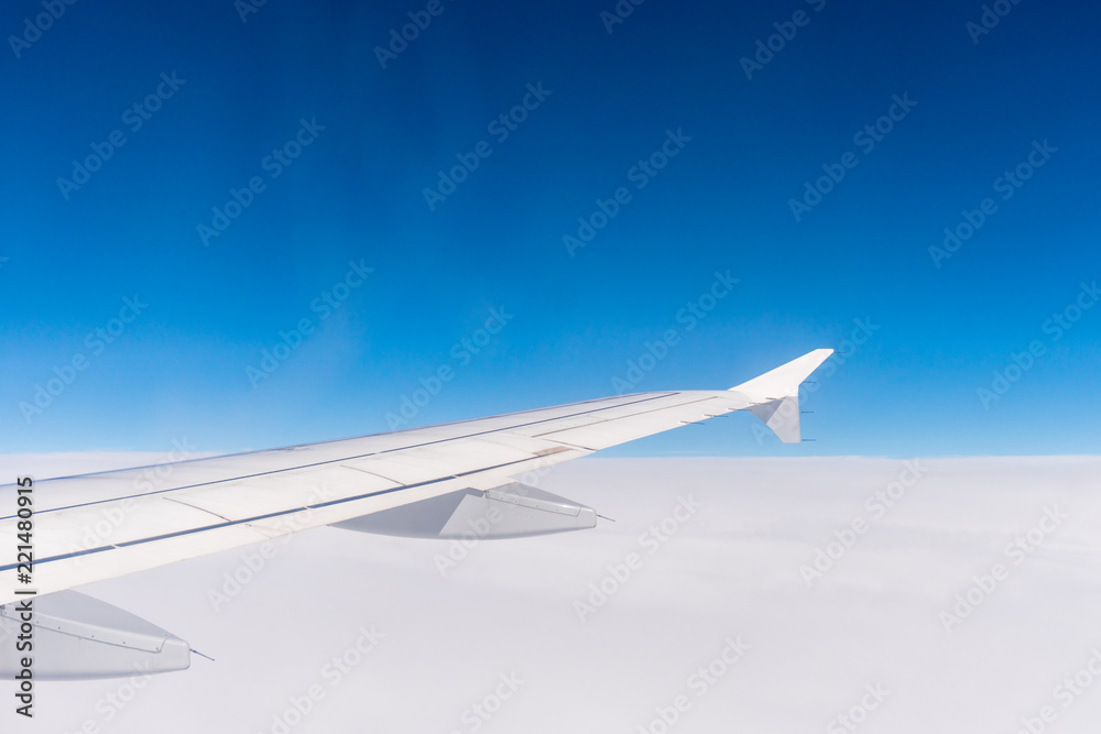 Fototapeta premium Wing of an airplane flying above the clouds. Window view of the blue sky. Aircraft wings.