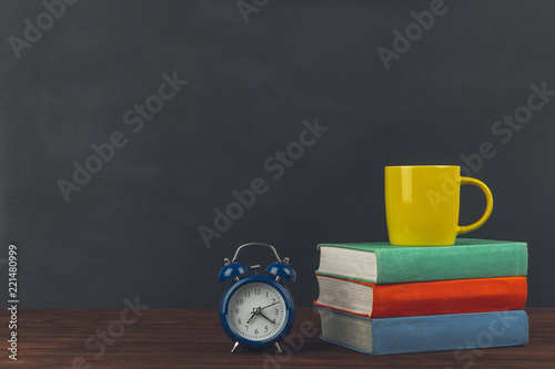 Stack of colorful textbooks on a wooden table, cup of coffee and alarm clock. Back to school.