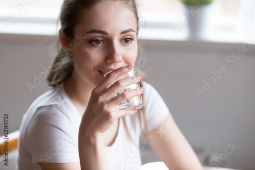 Fototapeta Naklejka Na Ścianę i Meble -  Thoughtful pretty millennial woman drinking pure water, dehydrated female holding glass feeling thirsty enjoying still mineral aqua, smiling girl thinking and refreshing. Healthy lifestyle concept.