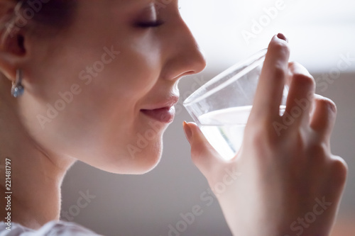 Fototapeta Close up of pretty female hold glass refreshing drinking pure mineral water in m