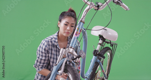 Asian woman fixing her bicycle on green screen