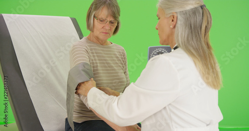 An older patient gets her blood pressure checked by her doctor on green screen
