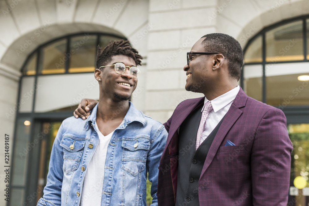 two young and stylish African American men in the city smiling and talking. father and adult son relationship two young and stylish African American men in the city smiling and talking. father and adult son relationship