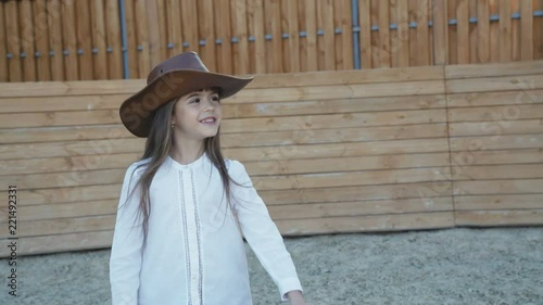 Cute little girl in hat walks and poses with smile on the hippodrome photo