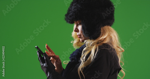 Caucasian woman in fur cap and scarf messaging on cellphone on green screen