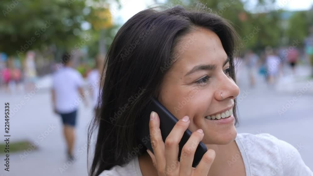Charming young lady with long dark hair talking by phone in the green spring alley, actively gesticulating and smiling. Modern communication, positive mood. Female portrait, close up Charming young lady with long dark hair talking by phone in the green spring alley, actively gesticulating and smiling. Modern communication, positive mood. Female portrait, close up