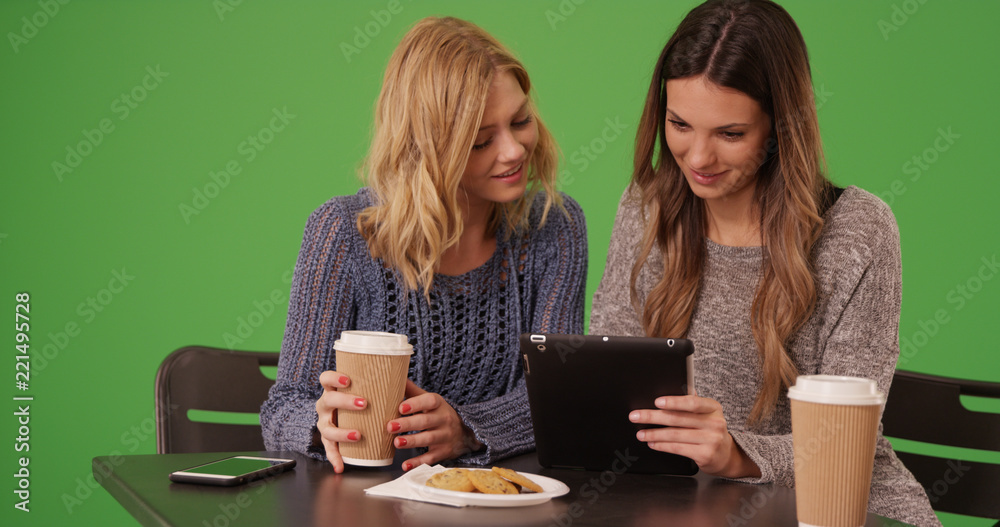 Couple of lovely girls sitting and sharing tablet computer on green screen