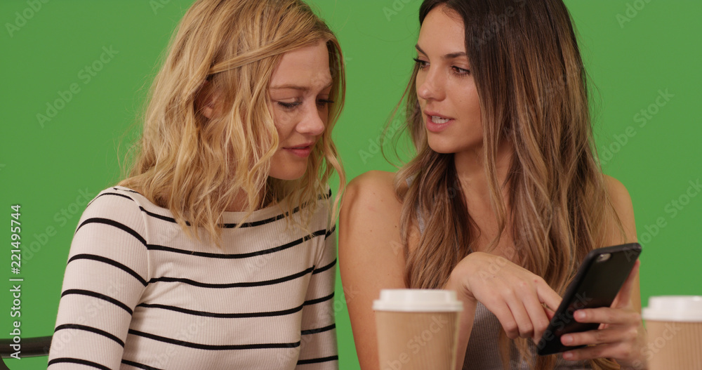 Pair of lovely women using mobile device together at cafe on green screen Pair of lovely women using mobile device together at cafe on green screen