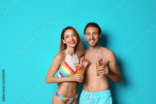 Happy young couple in beachwear with cocktails on color background