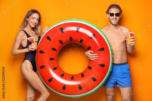 Happy young couple in beachwear with inflatable ring and cocktails on color background