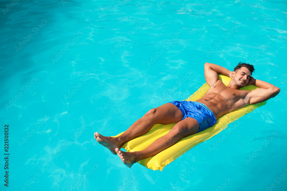 Young man with inflatable mattress in pool on sunny day