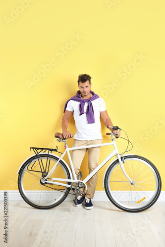 Handsome young hipster man with bicycle near yellow wall