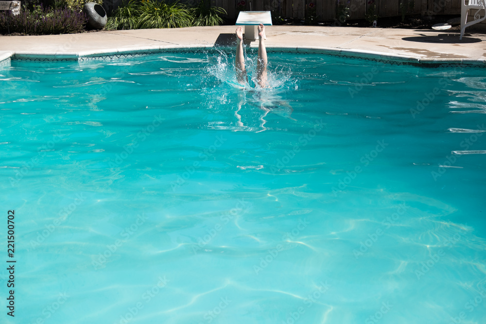 Woman jumping off a diving board into a swimming pool, legs above the water. Woman diving into