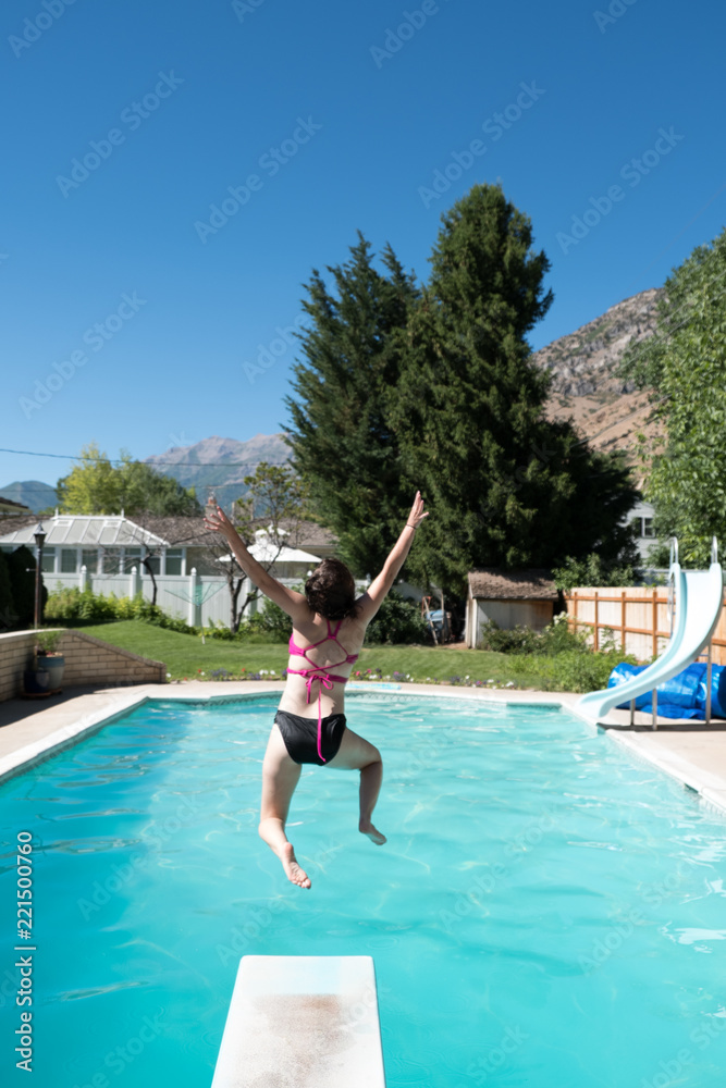 Young woman jumps off diving board into a backyard swimming pool. Woman entering the water after
