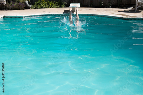 Woman jumping off a diving board into a swimming pool, legs above the water. Woman diving into an outdoor swimming pool in the summer.