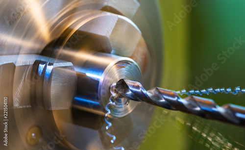 Drilling detail on a lathe with metal shavings. Close-up of a metallic workpiece clamped in a rotating machine chuck. Steel drill bit and twisted swarfes on a green background. Beautiful motion blur.