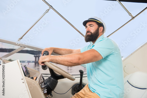 A young guy with a beard swims on the yacht at the helm