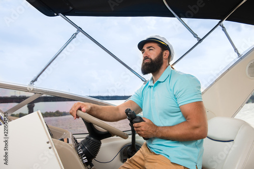 A young guy with a beard swims on the yacht at the helm