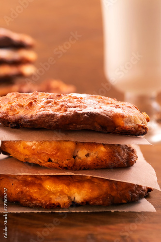 Cookies with a ruddy crust  stacked on top of each other in a column  a glass of milk  a wooden background  a vertical frame.