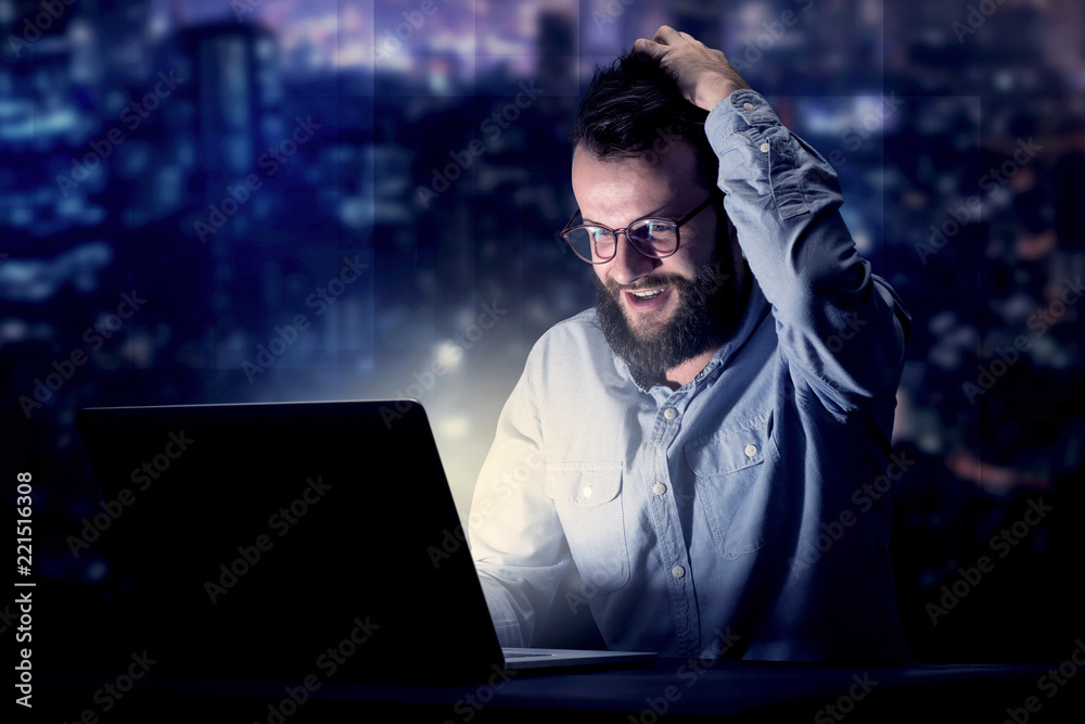 Young handsome businessman working late at night in the office with blue lights in the background Young handsome businessman working late at night in the office with blue lights in the background