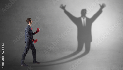 Businessman with boxing gloves fighting with disarmed businessman shadow 