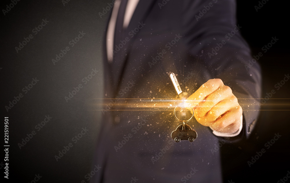 Businessman hand over shiny keys in dark suit with dark background
Businessman hand over shiny keys in dark suit with dark background