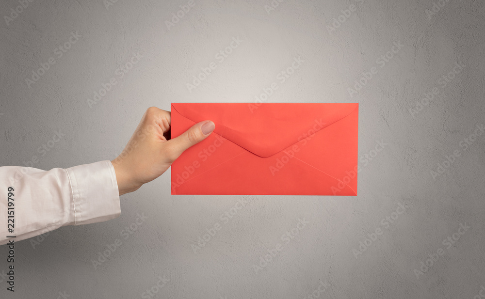 Female hand holding coloured and white envelope with empty wall background
