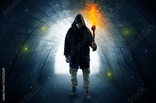 Ugly man with burning flambeau walking in a dark tunnel