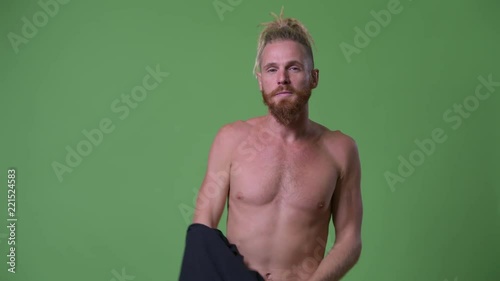 Handsome muscular bearded man with dreadlocks removing shirt