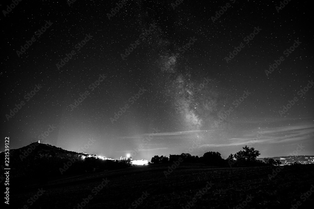 Beautiful view of starred night sky with milky way over a cultivated field Assisi town (Umbria, italy) in the background Beautiful view of starred night sky with milky way over a cultivated field Assisi town (Umbria, italy) in the background