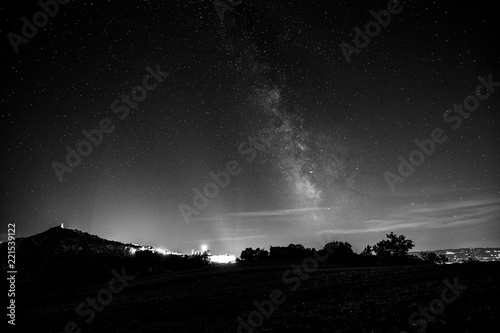 Beautiful view of starred night sky with milky way over a cultivated field Assisi town (Umbria, italy) in the background