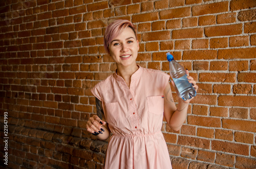 Young beautiful girl holds a bottle of water on a brick wall background