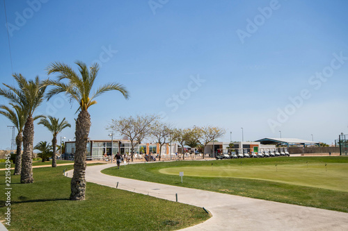 Golf clubhouse with palm trees, buggies and putting green at golf course in Spain on a summer day with clear blue sky