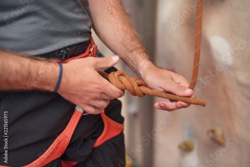 Rock wall climber wearing safety harness and climbing equipment indoor, close-up image