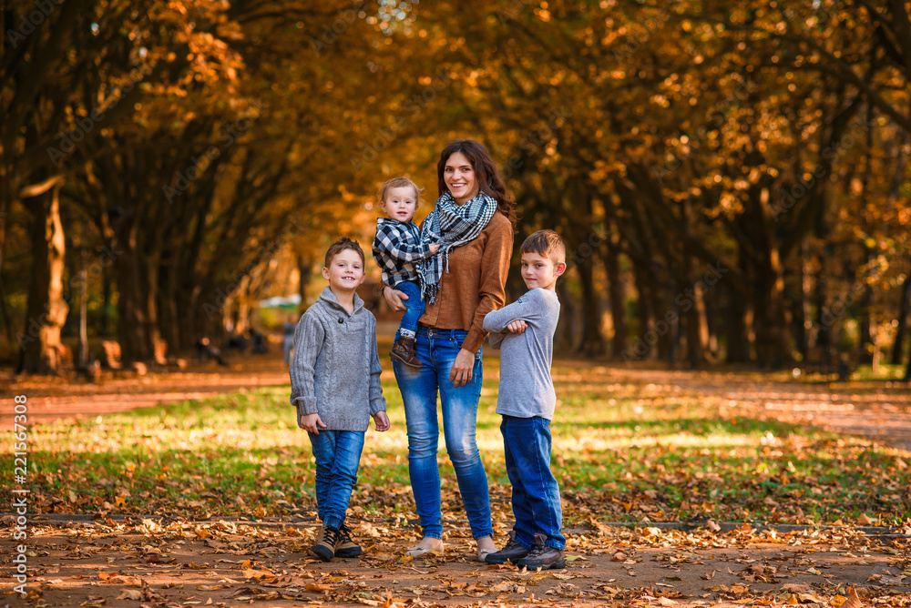 Young happy mother with her three smiling sons wearing denims and walking in the autumn park. Mom with her children on the autumn background.