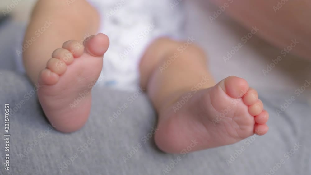 A close up of a baby naked feet. Her tiny toes are slowly moving while a baby is sitting on her parents lap A close up of a baby naked feet. Her tiny toes are slowly moving while a baby is sitting on her parents lap