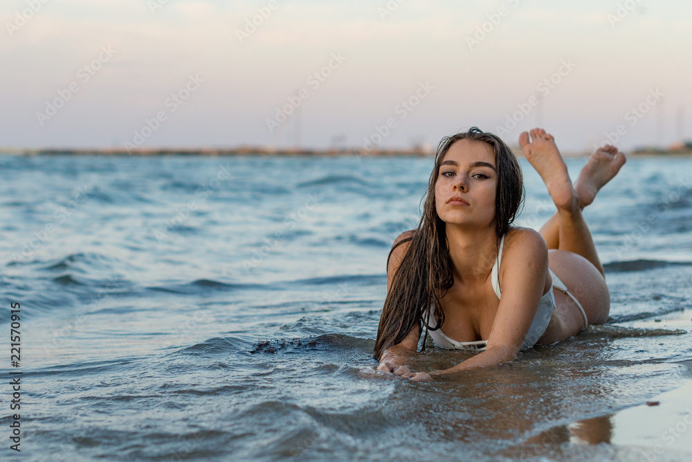 ragazza castana con costume bianco distesa nell'acqua sulla riva della  spiaggia di un mare italiano Photos | Adobe Stock