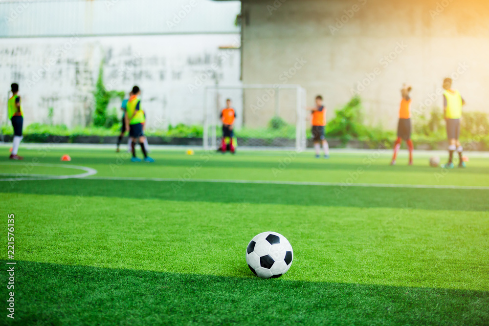 Football on green artificial turf with blurry soccer players background.