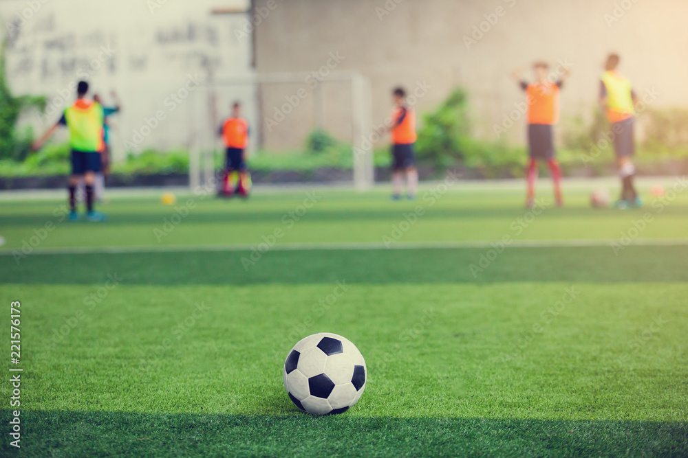 Football on green artificial turf with blurry soccer players background.