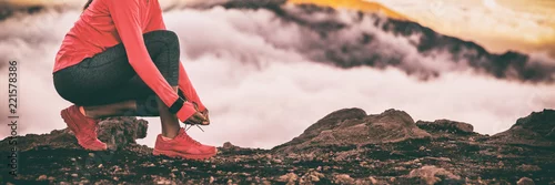 Obraz Biegacza smartwatch kobieta przygotowywa dla śladu bieg w wysokim zimnych chmur gór tle wiąże w górę butów do biegania koronki. Motywacja fitness i sport zdrowy styl życia. Przycinanie panoramiczne banerów.