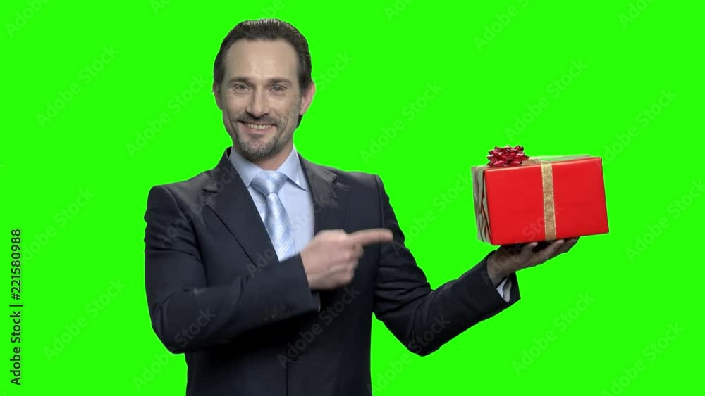 Businessman presents gift box. Pointing at red box. Portrait of man in suit on green screen hromakey background. Green hromakey background for keying. Businessman presents gift box. Pointing at red box. Portrait of man in suit on green screen hromakey background. Green hromakey background for keying.