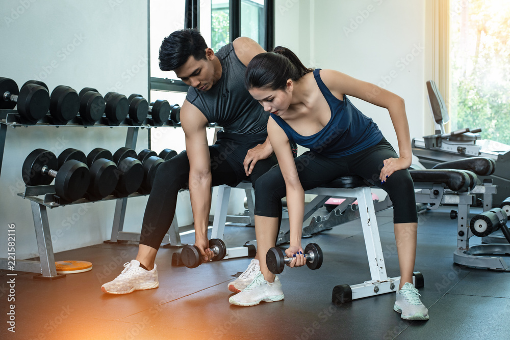 The beauty lady and handsome man are wearing exercise suit,prepare for lifting dumbbell up,for built arm muscle,at fitness room,blurry light around