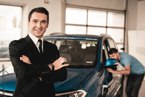 Car Dealer Camera Posing With Buyer On Background. © VadimGuzhva
