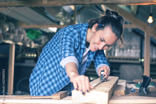 smiling woman in a home workshop measuring tape measure a wooden Board before sawing, carpentry