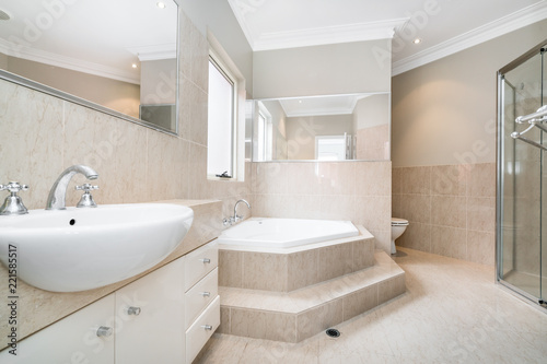 Large modern bathroom interior with floor to ceiling tiling  large bathtub  and luxury fittings.